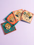 Set of four square ceramic coasters featuring a vampire cupid design in a pastel goth and traditional tattoo art style. The first coaster shows a fanged cherub on a teal background with red vines. The second features a cherub crying blood tears on a red background with daggers. The third depicts a cherub holding an anatomical heart on a peach background. The fourth shows a cherub with a spiked ring. Glossy glazed finish with cork backing. Ideal for spooky home decor and anti-valentine gifts.