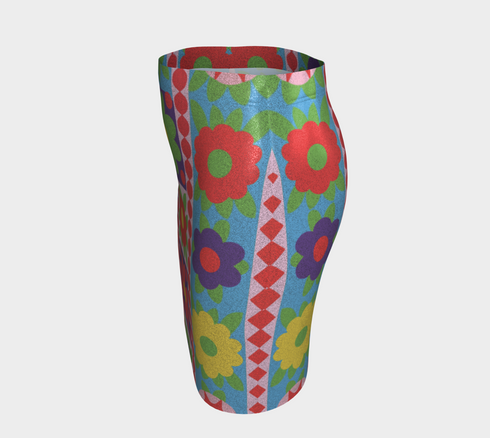 Form-fitting bodycon mini skirt with a mid-rise elastic waistband, falling to mid-thigh in smooth stretch fabric. It features a bold retro patchwork floral print: large mod daisies in red, purple, yellow, and green, set on a sky blue background with scattered green leaves. A central column frames single flowers on purple and pink tiles, edged by red and pink beaded borders. The all-over design is a flat dye-sublimated print, available in a smooth knit or glitter knit finish.