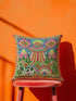 Description of a square throw pillow with a vibrant maximalist alien design. A central UFO with a large all-seeing eye hovers above a landscape with two rainbows, pink mountains, and green pine trees. A black and white spotted cow stands in the foreground. The design is a high-contrast palette of sky blue, magenta, hot pink, and meadow green. The pillow has a faux-embroidery 2D print finish on linen-feel fabric, framed by a yellow and pink scalloped floral border.