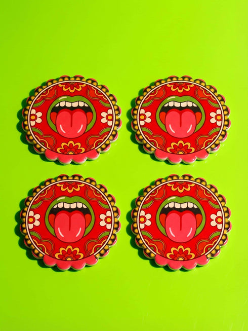 Round ceramic coaster with scalloped edges featuring a vibrant pop art design of an open mouth with green lips and a red tongue sticking out. The background is a bright red with psychedelic floral swirls in yellow orange and green. The surface is glossy glazed ceramic. The back is made of cork to prevent slipping. This maximalist decor piece fits retro 70s funky and weirdcore aesthetics. It is a bold statement piece for coffee tables. The design is colorful and eclectic dopamine decor.