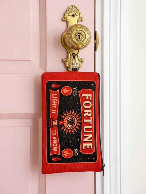 A rectangular red zippered pouch featuring a vintage-style tarot card design. The front displays the word FORTUNE in large beige capital letters. A central illustration shows a mystic eye emitting rays of light above a lit candle flame. The text YES and NO appears on the sides. A banner at the bottom reads LIGHT IT TO KNOW. The bag is crafted from red polyester with a linen-like woven texture, featuring a black zipper and a removable black nylon wrist strap. The interior is white.