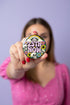 A round pinback button featuring a solid black background covered in a retro pastel colored design. The center reads 25TH NOW in a groovy bubbly font using pale pink and mint green referencing the 25th amendment. Surrounding the text is a maximalist cluster of cute but edgy motifs including smiling white skulls, pastel rainbows, pale yellow crescent moons, daisies, and a pink and white spotted mushroom. The button has a glossy laminate finish and a secure metal safety pin backing.