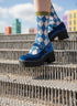A person's feet wearing blue and white checkered socks and blue velvet shoes are walking up a set of metal stairs.