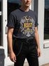 A unisex short sleeve graphic t shirt in dark charcoal black featuring a highly detailed symmetrical medallion print on the chest. In the center, the word RESIST is printed in a bold yellow gothic blackletter font. Two coiled white snakes with fine black scale details frame the text on the left and right. Above the text, a yellow crescent moon is flanked by white and yellow starbursts. Beneath, three yellow marigold flowers sit atop white stems and leafy foliage.
