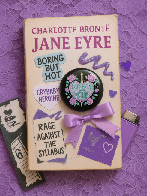 Glossy black pinback button featuring embroidered-style artwork of a pastel purple heart that reads “Read or Die” pierced by a sword and surrounded by roses; shown on books, graffiti, and lace backgrounds.