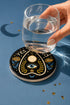 A close-up photograph of a glossy ceramic coaster featuring a Planchette occult design on a deep black background. The symmetrical graphic displays a central blue All-Seeing Eye with gold sunburst lines, topped by a white circle, and flanked by gold flowers with blue stems. At the top, the text "YES" is printed in gold on the left and "NO" on the right. Gold stars and crescent moons are scattered around the perimeter. The flat, round coaster has a highly visible high-gloss glaze.