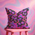 Throw pillow with a black background and a vibrant Y2K-inspired design featuring gradient cherries and shiny bows. The pattern includes pink, purple, orange, and blue psychedelic squiggles. The square pillow is displayed on a pink chair, bright blue couch, and outdoors with camping gear, emphasizing its bold, girly, and playful aesthetic. Perfect for dopamine decor, Gen Z bedrooms, or quirky home styling.