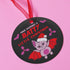 Round black metal Christmas ornament featuring cute pink bat with red wings wearing Santa hat, surrounded by pink bats and holly. Text reads "Have Yourself A Batty Little Christmas"