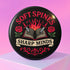 A round pinback button in black with a glossy mylar face and metal construction. The design, in a traditional tattoo style, features a central open book with flames rising from its pages. Two silver swords with black hilts are crossed over the book. On either side of the book is a red rose with a green stem and leaves. Below the book is a cream-colored banner with the words "SHARP MINDS" in a black serif font. Above the book, the words "SOFT SPINES" are written in a curved, red font.