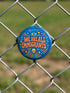 A round 1.75 inch blue pinback button featuring retro psychedelic artwork. The text reads We Are All Immigrants in a groovy orange and red 1970s font style centered on the badge. A mystic third eye sits above the text while a small skull sits below it. Wavy rainbow lines in cyan, green, and orange radiate outward from the center along with small starbursts and lightning bolts. The button has a glossy finish reflecting light.