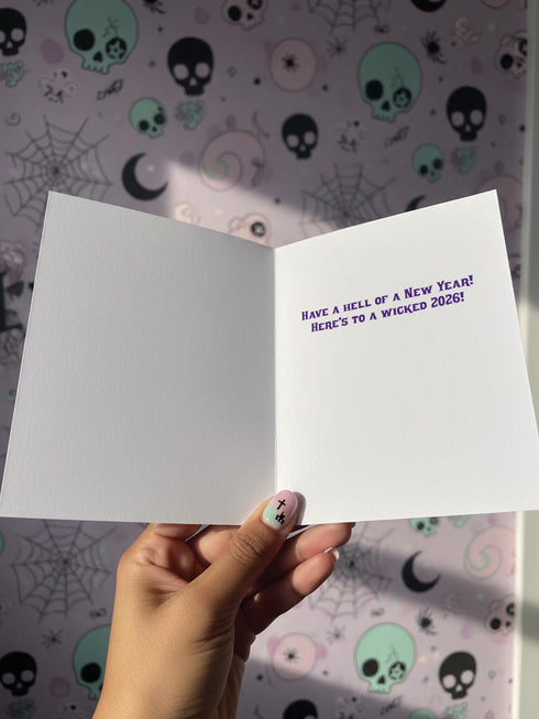 A vertical 5x7 inch folded greeting card featuring a detailed, psychedelic illustration of the folklore figure Krampus for a New Year celebration. The card stock has a shimmering pearlescent finish that reflects light, creating a glowing effect on the purple and teal artwork. The design mimics a vintage event poster reading "Krampus Ball 2026" and "Entry Fee: One Naughty Soul" in retro fonts. Krampus is depicted with large horns, sunglasses, and a long tongue holding a candy cane.