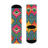 Crew-length socks featuring a vibrant 70s psychedelic pattern on a dark emerald green background. The design consists of vertical symmetrical medallions with hot pink scalloped edges, royal blue interior teardrops, and safety orange accents at the top ribbing. Fine white and light blue pointillist dots outline the major shapes. The heel and toe are solid black and reinforced. The fabric is a smooth. The pattern is maximalist and colorful, showcasing a retro aestheti.
