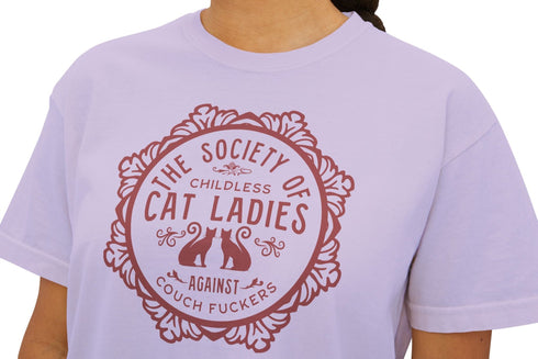 The Society of Childless Cat Ladies Against Couch Fuckers" 2024 election T Shrort design featuring two cats in an ornate circular frame, available in white and purple.