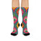 Crew-length socks featuring a vibrant 70s psychedelic pattern on a dark emerald green background. The design consists of vertical symmetrical medallions with hot pink scalloped edges, royal blue interior teardrops, and safety orange accents at the top ribbing. Fine white and light blue pointillist dots outline the major shapes. The heel and toe are solid black and reinforced. The fabric is a smooth. The pattern is maximalist and colorful, showcasing a retro aestheti.