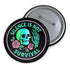 Round enamel pinback button available in 2.5″ or 3″ sizes with a black base and high-gloss finish. The design features neon green and blue gradient skull in the center, pastel pink roses and green leaves below, and mint skeleton hand on the right side. Arched text reads “SILENCE IS NOT SURVIVAL” in teal block letters. Shown styled on a denim jacket, held in hand against bright yellow backdrop, placed in a candy heart flat lay, and propped on pavement in front of graffiti wall.