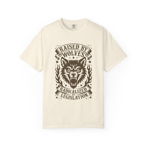 Vintage style graphic t-shirt with a large snarling wolf face printed in dark charcoal ink. A curved banner above reads RAISED BY WOLVES and a banner below reads RADICALIZED BY LEGISLATION, framed by stylized flames and scattered stars. Classic crewneck short sleeve cotton tee with a relaxed fit and seamless sides, available in soft pink, pale green, and ivory. Feminist protest apparel and activist statement tee for reproductive rights, marches, and everyday quiet rage.