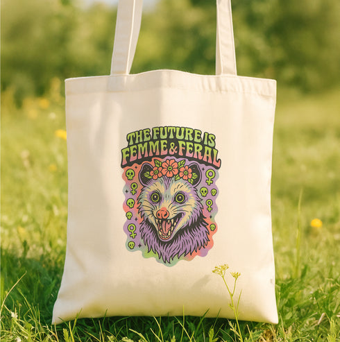 A white tote bag with a colorful graphic design featuring a cartoon-like creature with a flower in its mouth, surrounded by various symbols and text.