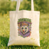 A white tote bag with a colorful graphic design featuring a cartoon-like creature with a flower in its mouth, surrounded by various symbols and text.