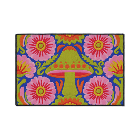 A rectangular polyester mat featuring a large central mushroom with a lime green cap, orange spots, and a pink underside. The design is surrounded by four large magenta and pink radial flowers with yellow centers. Bright green leaves and orange scrolling vines fill the spaces on a deep cobalt blue background. The artwork uses a tapestry-style visual effect to mimic the look of raised embroidery on a flat, printed surface. The mat is finished with a clean black stitched edge.