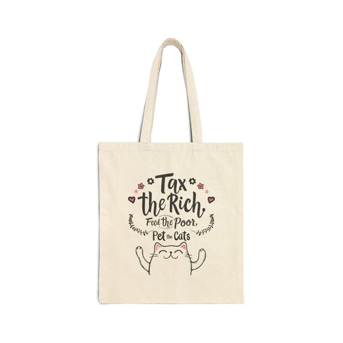 A natural-colored cotton canvas tote bag featuring a bold pink design with a cartoon cat illustration and the phrase “Tax the Rich, Feed the Poor, Pet the Cats.” The artwork is printed on the front side of the bag, which measures 15 inches by 16 inches. The bag includes two sturdy handles for carrying and is made from eco-friendly cotton material, designed for everyday use as a book tote, protest bag, or gift for anti-capitalist cat lovers.