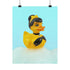 A chic rubber duck styled like Audrey Hepburn’s Holly Golightly, wearing a high bun, yellow bow, black gloves, and a sparkly choker. The duck floats in a pile of foam and is framed in white on a bubbly bathroom shelf with a red tile backdrop and soap dispenser.