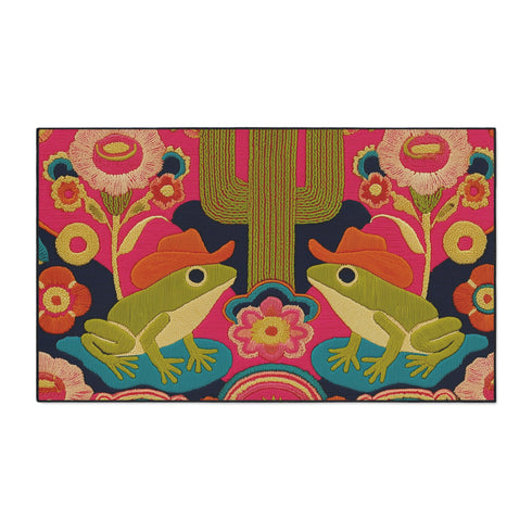 A rectangular polyester doormat with a black trim and non-slip rubber backing. The vibrant, colorful design features a symmetrical illustration on a dark navy blue background. In the center, two green frogs wearing orange cowboy hats sit facing each other. Between them is a tall, olive-green saguaro cactus. The scene is filled with large, psychedelic-style flowers in hot pink, orange, and yellow. The overall aesthetic is funky, retro 70s, maximalist, and trippy, mimicking the look of embroidery.