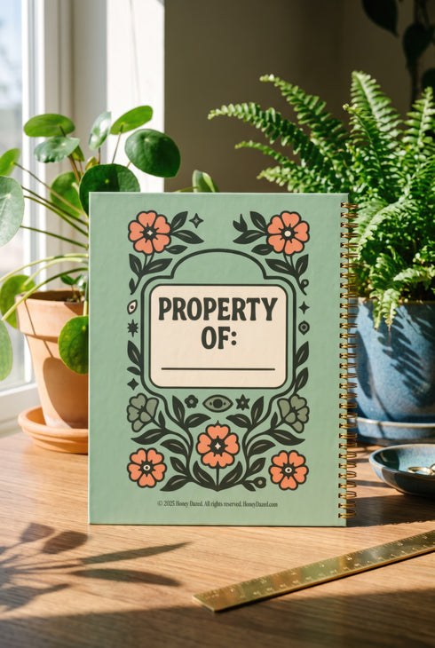 A sage green hardcover spiral planner for 2027-2028 with the title "The 2027 Planner of Controlled Chaos" in a funky, retro 70s-style font. The cover features a groovy illustration of orange and pink flowers in a vase, with one flower depicted as an eyeball. The text reads "Bloom where you're planted. Or just wilt artfully." and "Notes from the Void." The planner has a gold metal wire-o binding. The back cover shows a decorative floral frame with a "Property Of" section