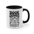 A two-tone ceramic mug with a glossy white exterior and a contrasting black interior, handle, and rim. The front of the mug features a black, rectangular graphic with the words "BOOK COVEN" in a bold, wavy, 70s-inspired retro font. Below the text is an occult-style illustration of an open book on a stand. An all-seeing eye with a snake coiled around it emerges from the book's pages, radiating lines of light. Smaller books float around the central image, completing the witchy, bookish design