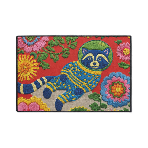 A rectangular outdoor doormat featuring a maximalist 2D print with a Trompe-l'œil embroidery effect. The central design depicts a blue and gold patterned raccoon wearing a green astronaut space helmet. The background is a vibrant red, filled with large, multi-colored folk art flowers in shades of pink, magenta, and gold with green leaves. The mat is finished with a sleek black border and has a textured surface mimicking high-fidelity raised needlepoint stitching.