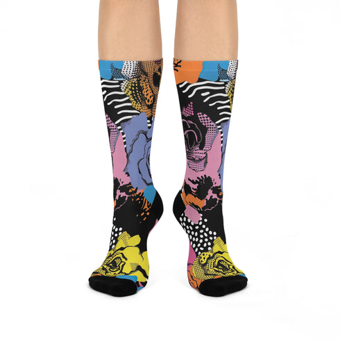 Colorful crew-length socks with a vibrant floral pop-art collage design, featuring abstract roses in yellow, lavender, pink, and orange tones, polka dots, and zebra stripes on a black background.