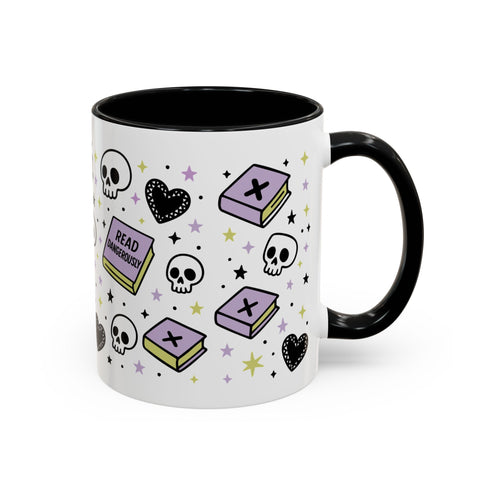 The Gothic Read Dangerously Mug (11 or 15oz) is a glossy white ceramic coffee mug with a black handle/interior, featuring pastel purple books, skulls, black hearts, stars, and “READ DANGEROUSLY!” in bold. BPA-free.