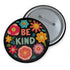 Bold "BE KIND" pinback button featuring vibrant psychedelic flowers in hot pink, teal, yellow, and orange on black background. Retro 70s-inspired typography in coral and mint green surrounded by colorful blooms. Statement activist accessory perfect for punk fashion, protest wear, and battle vests. Glossy UV-resistant finish with safety pin backing available in 2" and 3" sizes.