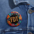Circular black pinback button with bright 'FDT' lettering in orange/teal surrounded by colorful embroidery-style flowers in red, purple, blue, and yellow. Metal safety pin backing visible on reverse side. Political protest pin with vibrant Mexican folk art-inspired floral design.