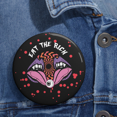 Black circular pin badge with purple fanged mouths design, psychedelic orange spiral, and "EAT THE RICH" text in white, scattered with red dots