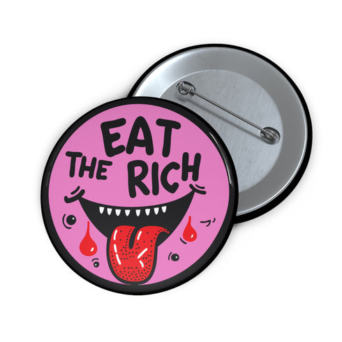 Round pink pinback button featuring a cartoon-style open mouth with sharp teeth, a red tongue, and dripping red details. The bold black text reads “EAT THE RICH” in a hand-drawn style. Glossy black rim with a vibrant, rebellious graphic design.