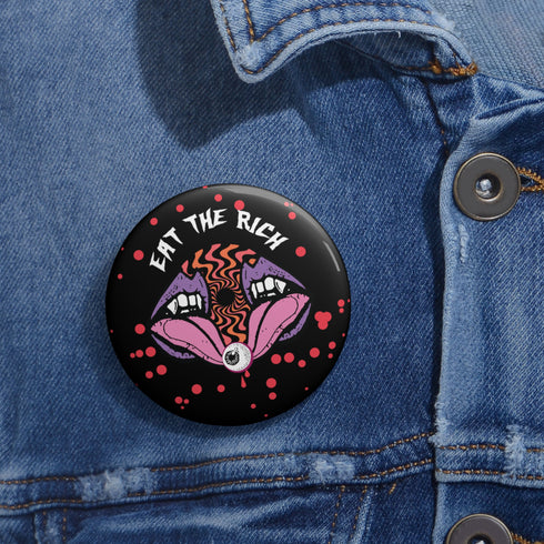 Black circular pin badge with purple fanged mouths design, psychedelic orange spiral, and "EAT THE RICH" text in white, scattered with red dots
