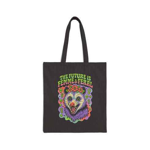 Black or natural cotton canvas tote bag with “The Future is Femme & Feral” design featuring a rainbow-colored snarling opossum with flowers and feminist symbols, printed on both sides with long matching canvas handles.