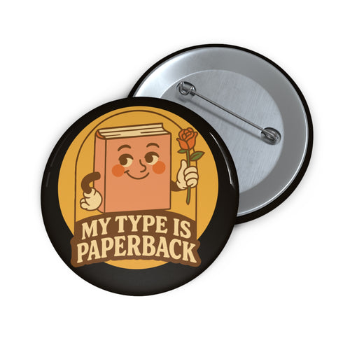 A glossy black round pin-back button with a retro 1970s-style design. The center shows a smiling cartoon paperback book holding a red rose, colored light brown with white gloves and feet. Below, “MY TYPE IS PAPERBACK” appears in chunky brown-and-tan 70s lettering. This bookish flair piece has a high-gloss, scratch-resistant mylar finish, secure safety pin backing, and comes in two- or three-inch sizes.