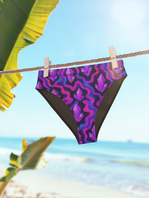 High-waisted bikini bottom with a psychedelic crystal pattern in purple, magenta, and black, featuring cheeky cut and four-way stretch fabric with a moisture-wicking finish.