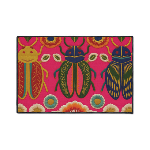 A rectangular doormat featuring a vibrant hot pink background with a high-fidelity tapestry-style print of three large, detailed beetles. The central beetle is emerald green and gold with navy accents, flanked by two side-profile beetles in ochre and deep blue. Stylized teal and yellow sunburst flowers and small sage green leaves are scattered throughout the design. The mat has a sleek black-trimmed edge and a visible flat, durable polyester texture mimicking intricate needlework.