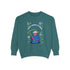 A holiday sweatshirt featuring a cute Grim Reaper holding a scythe, wearing a Santa hat. Above the character is the text "Grave Tidings We Bring," surrounded by festive snowflakes and holiday-themed designs. The combination of spooky and festive elements adds a humorous twist to traditional holiday attire.