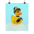 A chic rubber duck styled like Audrey Hepburn’s Holly Golightly, wearing a high bun, yellow bow, black gloves, and a sparkly choker. The duck floats in a pile of foam and is framed in white on a bubbly bathroom shelf with a red tile backdrop and soap dispenser.