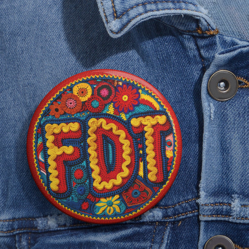 Round pinback metal button featuring an embroidered-style design on a vibrant, multicolored background. The bold, textured letters "FDT" are prominently displayed in red with intricate golden-yellow stitching details, outlined in dark blue. Surrounding the text is an ornate floral pattern with embroidered-style flowers in shades of red, orange, blue, and yellow, densely arranged for a rich, decorative effect. The outer edge is bordered with a zigzag stitching effect in red and blue. The button's back is sil