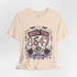 A short sleeve unisex crewneck t-shirt featuring a detailed Moon Tide 8647 graphic centered on the chest. The design includes bats, crescent moons, and spiderwebs at the top, with Moon Tide in a dripping font above a large 8647 rendered in shell patterned bubble numbers. The bottom features a skull inside a scallop shell, roses, and a Saltwater Spell banner. The color palette uses mint green, lilac, and salmon pink with black outlines. The shirt is shown in light pink, lavender, and cream.