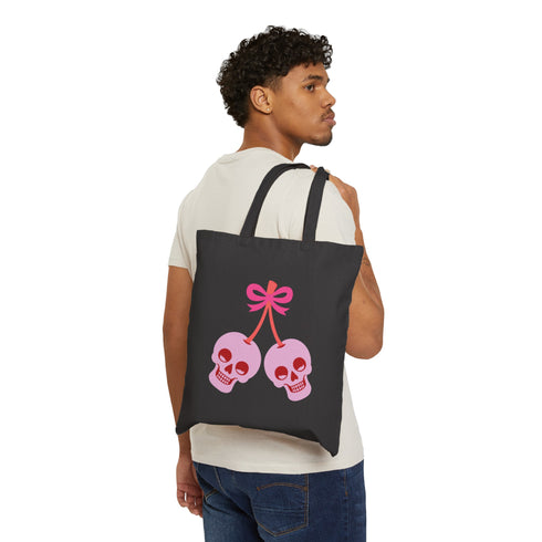 Canvas tote bag featuring pink skull cherries design. Two pink skulls connected by red stem and bow. Quirky gothic-inspired graphic on cream background. Stylish, edgy accessory for everyday use. Perfect for alternative fashion lovers.