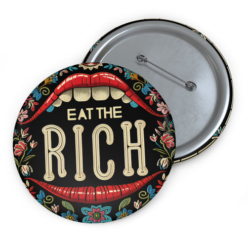 A round pin-back button with a bold, embroidered-style design featuring the phrase "EAT THE RICH" in large, vintage-style lettering. The typography is framed by a set of open red lips with detailed stitching, revealing white teeth. Surrounding the mouth are intricate floral patterns in shades of blue, red, and green, adding a decorative, folk-art-inspired touch. The button has a black background, making the details and lettering stand out