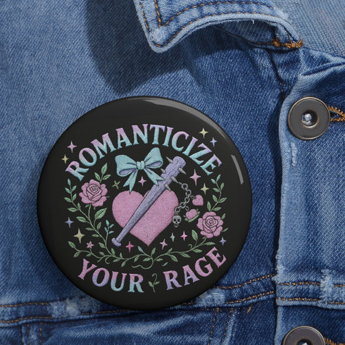 Glossy black pinback button featuring pastel gothic artwork with the phrase "Romanticize Your Rage" in bold white and lavender lettering. The design includes a pink glitter heart, a silver dagger, mint green bow, roses, stars, and delicate vines. Styled against a pink and purple gradient background, this round button blends soft romantic visuals with fierce messaging, perfect for pastel goth, feminist, or alternative fashion aesthetics.