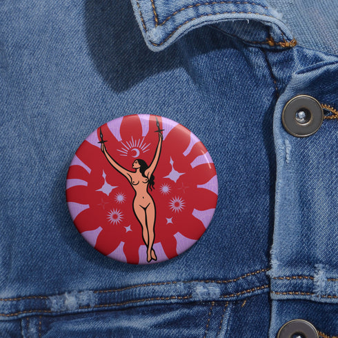 Circular pin featuring a nude goddess figure in gold against a red sunburst pattern on lavender background, with moon and star details
