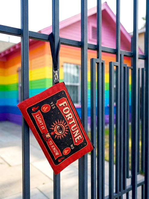 A rectangular red zippered pouch featuring a vintage-style tarot card design. The front displays the word FORTUNE in large beige capital letters. A central illustration shows a mystic eye emitting rays of light above a lit candle flame. The text YES and NO appears on the sides. A banner at the bottom reads LIGHT IT TO KNOW. The bag is crafted from red polyester with a linen-like woven texture, featuring a black zipper and a removable black nylon wrist strap. The interior is white.