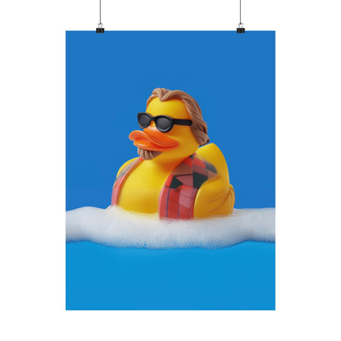 A quirky art print of a rubber duck styled after The Dude from The Big Lebowski, complete with a goatee, sunglasses, and plaid bathrobe. The duck lounges in bubbles, framed in a glossy red frame, with a manicured hand adjusting it against a monochromatic red backdrop.